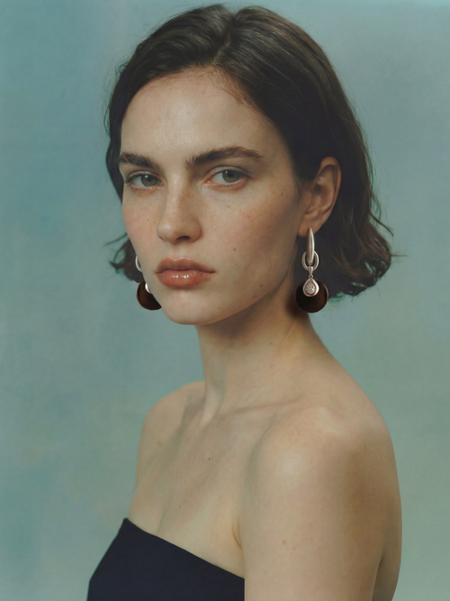 Model wearing MOUNSER Crespi Earrings in Ink Lacquer with obsidian disc and cubic zirconia teardrop charms, styled with a navy strapless top against a teal background.