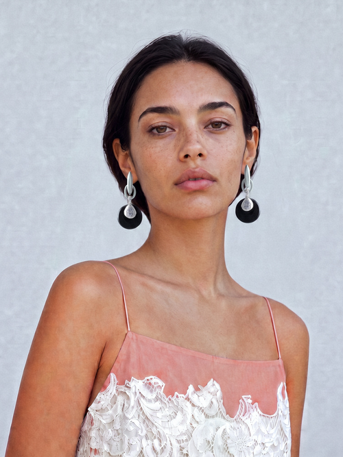 Model wearing MOUNSER Crespi Earrings in Ink Lacquer with obsidian disc and cubic zirconia teardrop charms, styled with a navy strapless top against a teal background.