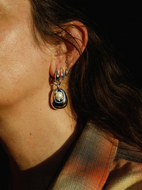 Woman wearing MOUNSER Tide Pool Earrings, sculptural silver freshwater pearl drop earrings on a huggie hoop, from the Seascape Abstracted Collection