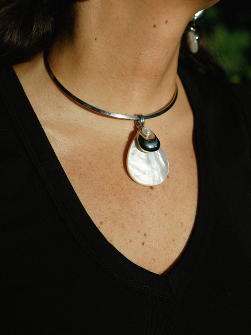 Close-up of the MOUNSER Half Shell Necklace worn on the collarbone, showing the mother-of-pearl shell pendant and freshwater pearl accent in detail