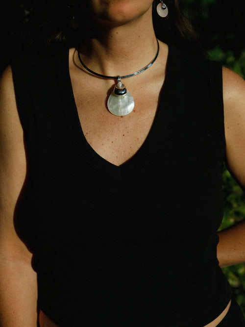 Woman wearing the MOUNSER Half Shell Necklace, a sculptural mother-of-pearl pendant with freshwater pearl and silver accent on a fixed collar, from the Seascape Abstracted Collection