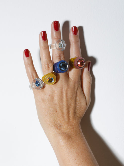 Hand shot of MOUNSER Bliss Ring in Honey a delicate and minimal acrylic cocktail ring in a jewel toned palette with a Swarovski crystal gemstone.  