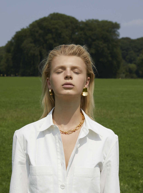 outdoor shot of MOUNSER Peel Earrings in Gold sxculptural statement wave shaped earring