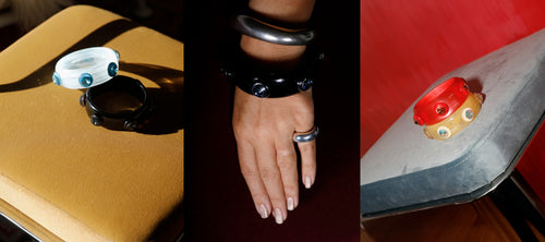 Three styled shots of MOUNSER Ambrosia Sculptural Resin Bangles in blue, black, red and yellow colorways with Swarovski Austrian crystal gemstone studs, shown on a tan leather surface, worn stacked on wrist with sterling silver ring, and resting on a chrome chair against a red background, handcrafted art object jewelry made in Los Angeles.