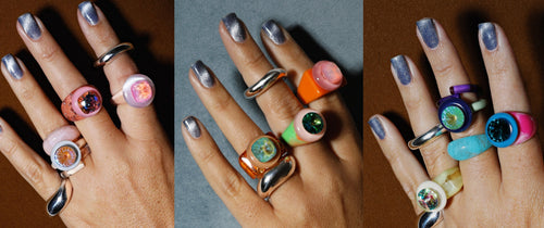 Three hands wearing stacked MOUNSER colorful crystal resin rings in pink, peach, orange, green, blue and purple colorways with iridescent Swarovski crystal gemstone centers, handcrafted art object jewelry made in Los Angeles.