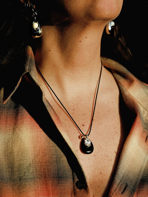 Model wearing MOUNSER Nereid Necklace in Lava colorway with obsidian pendant and gold-plated brass crystal setting on twisted silk cord.