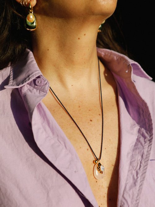 Close up of model wearing MOUNSER Nereid Necklace in Conch colorway, rose quartz pendant with gold-plated brass crystal setting resting at neckline on twisted silk cord.