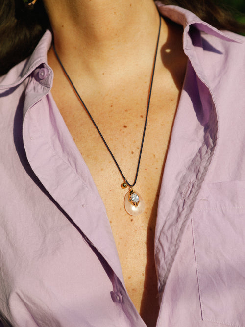 Model wearing MOUNSER Nereid Necklace in Conch colorway with rose quartz pendant and gold-plated brass crystal setting on twisted silk cord, styled with a lavender shirt.