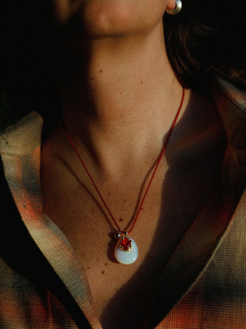Close up of model wearing MOUNSER Nereid Necklace in Conch colorway, rose quartz pendant with gold-plated brass crystal setting resting at neckline on twisted silk cord.