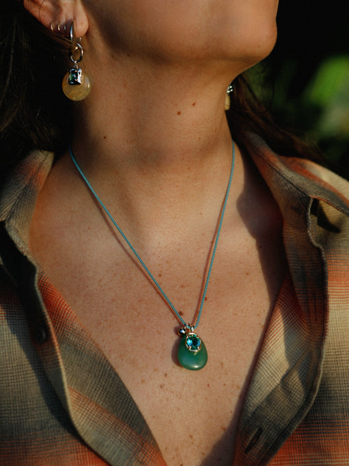 Model wearing MOUNSER Nereid Necklace in Lagoon colorway with 
aventurine pendant and gold-plated brass crystal setting on twisted silk cord.