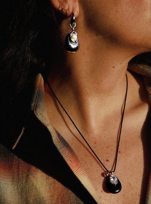 Close up of model wearing MOUNSER Nereid Necklace in Lava colorway, Obsidian pendant with gold-plated brass crystal setting resting at neckline on twisted silk cord.