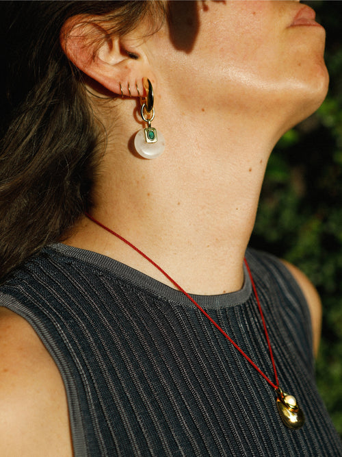 Side profile of model wearing MOUNSER Tide Pool Necklace with sculptural gold-plated brass freshwater pearl pendant on crimson twisted silk cord, styled with dark ribbed top and gold hoop earring.