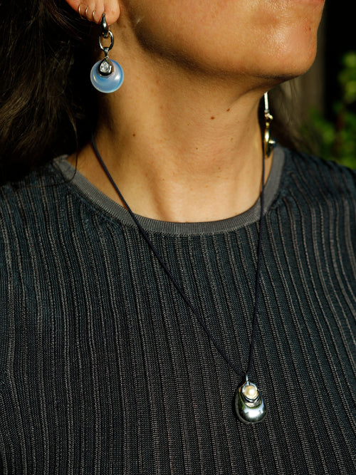 Model wearing MOUNSER Tide Pool Necklace with sculptural silver-plated brass freshwater pearl pendant on crimson twisted silk cord, styled with a dark ribbed sleeveless top.
