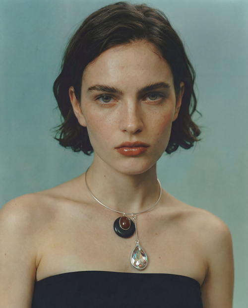 Model wearing the MOUNSER Rega Collar Necklace in Caviar with stacked obsidian and crystal pendants, styled with a black strapless top against a teal background.