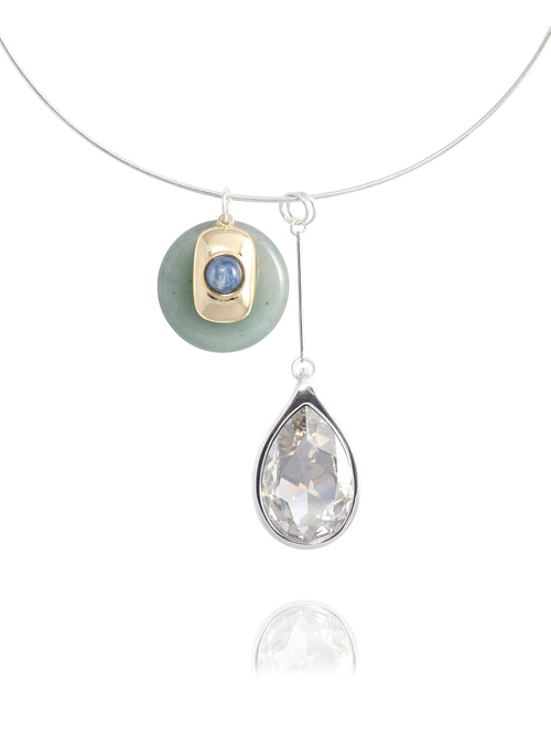 Close-up detail of the MOUNSER Rega Collar Necklace in Cucumber showing the jade disc with blue kyanite and 14k gold-plated brass accent above an elongated clear Austrian crystal teardrop in rhodium-plated brass setting, with reflection.