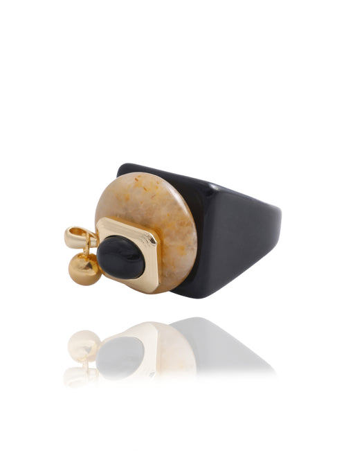Side angle detail of the MOUNSER Rizzo Ring in Caramel showing the 14k gold-plated brass orb charm, jade disc, obsidian oval element, and glossy black acrylic resin band with reflection.