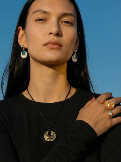 Model wearing MOUNSER Caspian Ring in Papaya - orange resin ring with yellow jade and citrus crystal teardrop charm styled with Isle Earrings in Sea Spray and MOUNSER necklace against blue sky