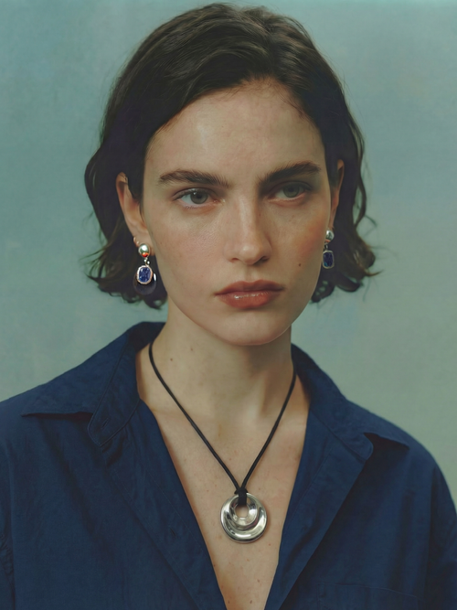Model wearing MOUNSER Isle Earrings in Abyss - obsidian disc and sapphire Austrian crystal drop earrings with sterling silver post styled with coordinating MOUNSER necklace against mint green background