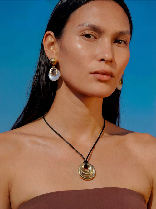 Model wearing MOUNSER Isle Earrings in Celeste Opal with coordinating MOUNSER necklace - sculptural opalite glass and gray Austrian crystal drop earrings with 14k gold-plated post against blue sky