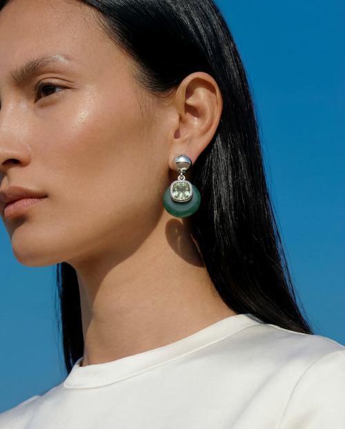 Close up of model wearing MOUNSER Isle Earrings in Comber Green - sculptural green jade and light green Austrian crystal drop earrings with sterling silver ball post against blue sky