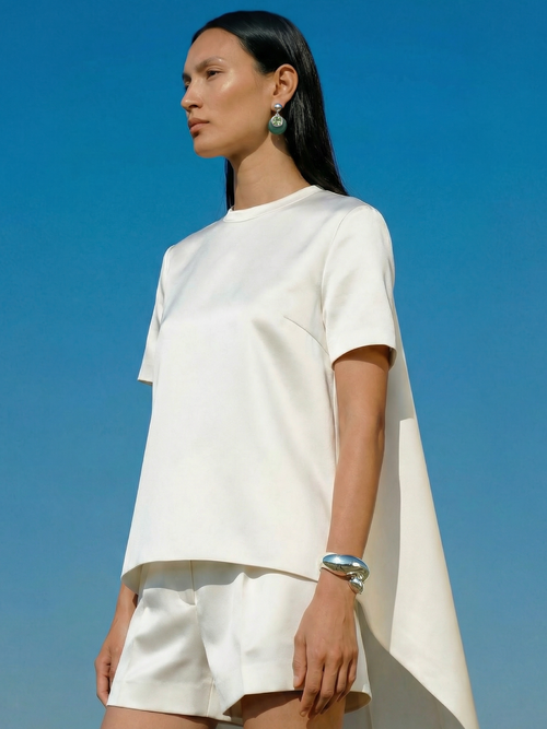 Model wearing MOUNSER Isle Earrings in Comber Green styled with white outfit and silver cuff bracelet against blue sky - sculptural green jade and crystal drop earrings