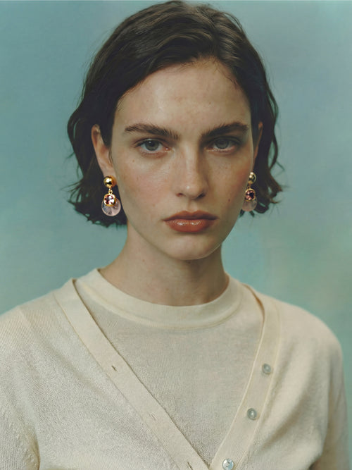 Model wearing MOUNSER Isle Earrings in Conch Pink - rose quartz and pink crystal sculptural drop earrings with gold post styled with cream knitwear