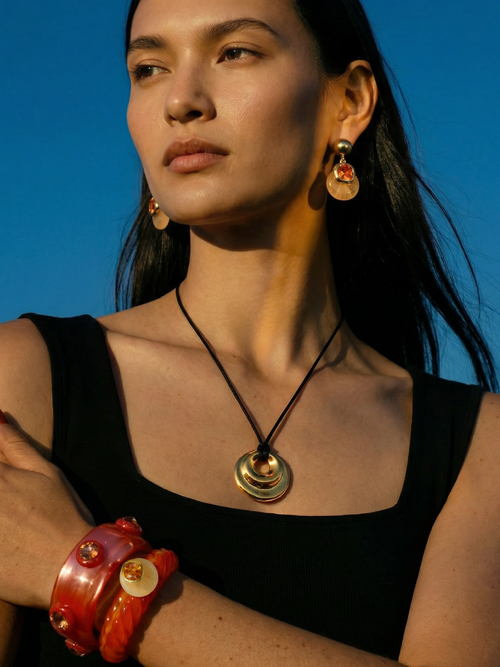 Model wearing MOUNSER Isle Earrings in Papaya - yellow jade and citrus orange Austrian crystal drop earrings with 14k gold-plated post styled with MOUNSER necklace and bracelets against blue sky