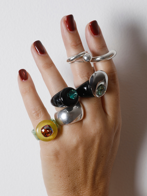 Hand wearing the MOUNSER Orbital Ring in Charcoal on the finger among multiple rings, showing the black agate disc’s size and scale.