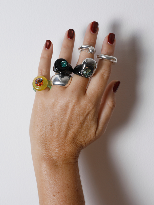 Close-up of the MOUNSER Orbital Ring in Charcoal on hand: black agate disc pierced with a mini faceted green crystal moon.