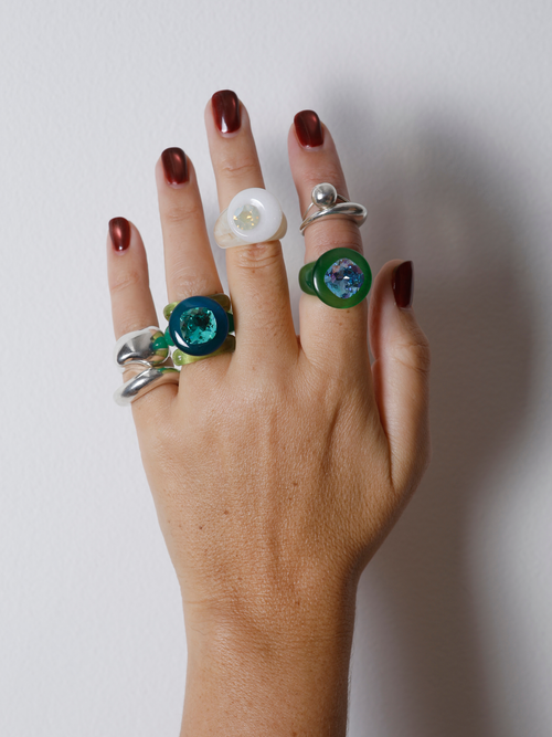 Close-up of the MOUNSER Orbital Ring in Griege on hand: white jade disc pierced with a mini faceted white crystal moon.