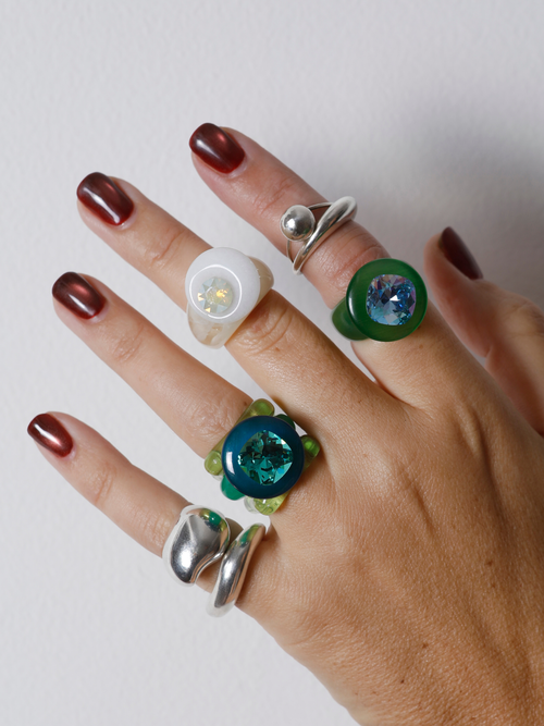 Hand wearing the MOUNSER Orbital Ring in Griege on the finger among multiple rings, showing the white agate disc’s size and scale.