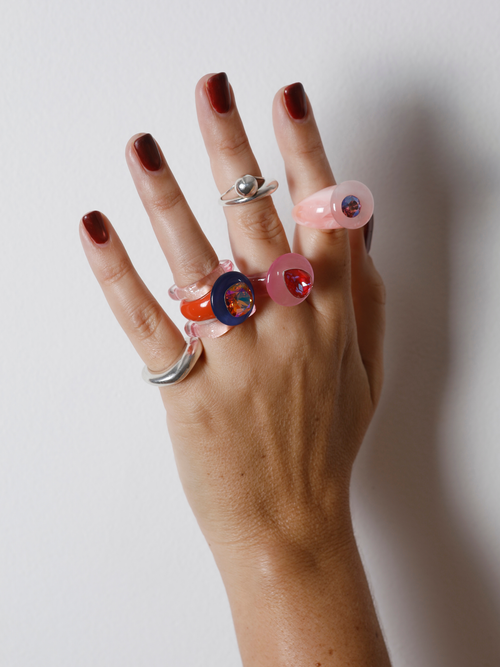 Hand wearing the MOUNSER Orbital Ring in Pink Aurora on the finger among multiple rings, showing the carnelian disc’s size and scale.