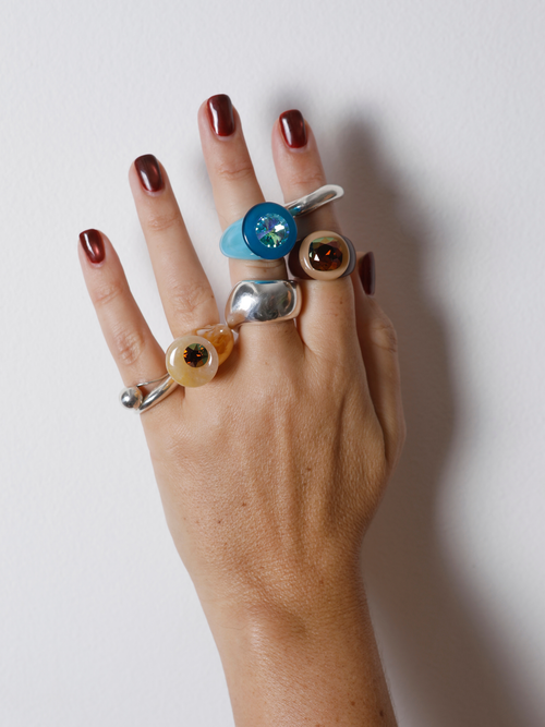 Hand wearing the MOUNSER Orbital Ring in Silica on the finger among multiple rings, showing the yellow jade disc’s size and scale.