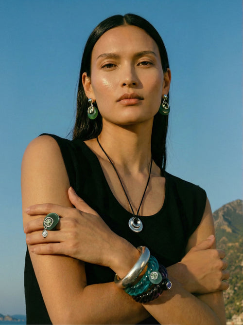 Model wearing MOUNSER Scallop Cuff in Comber Green - deep green resin cuff with jade and crystal styled with Isle Earrings in Comber Green MOUNSER necklace ring and bracelet stack against blue sky