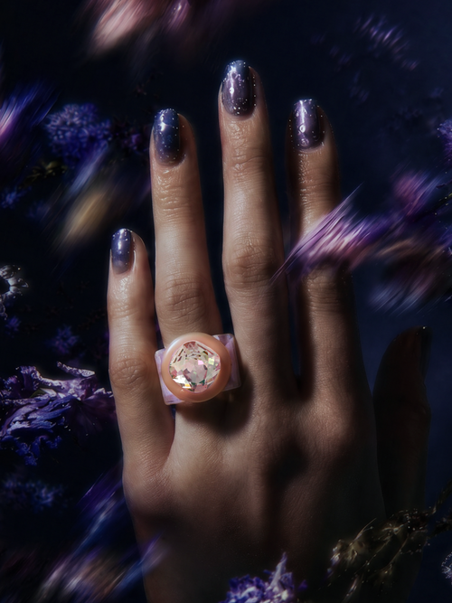 MOUNSER Spectrum Ring in Ballerina worn on model's hand — milky pastel pink limited edition cocktail ring with iridescent Austrian crystal on a dark purple floral background,  art object jewelry handcrafted to order in Los Angeles.