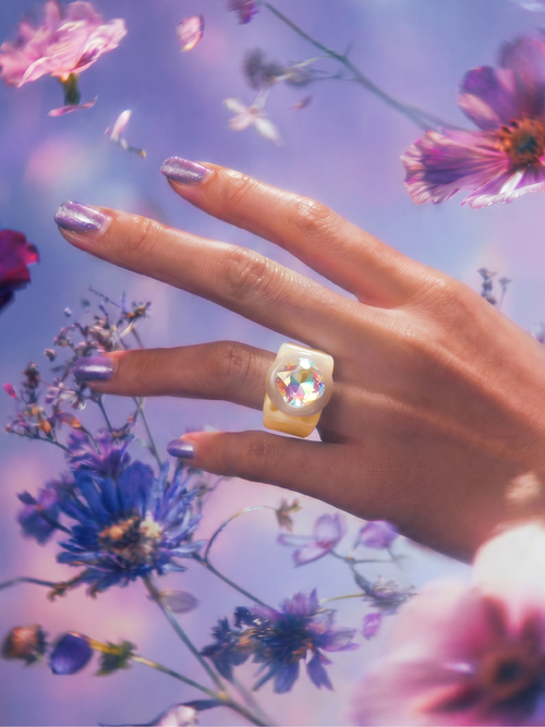 MOUNSER Spectrum Ring in Blonde worn on model's hand — milky light peach limited edition cocktail ring with iridescent Austrian crystal on a purple floral background,  art object jewelry handcrafted to order in Los Angeles.