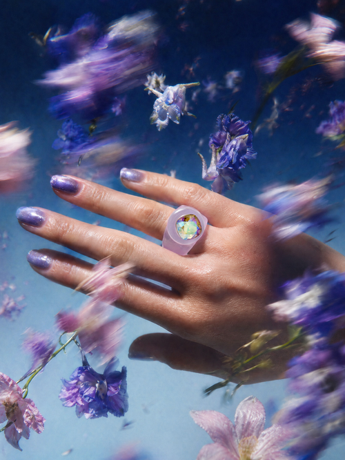 MOUNSER Spectrum Ring in Eyeshadow worn on model's hand — milky lavender limited edition cocktail ring with iridescent Austrian crystal on a dark purple floral background,  art object jewelry handcrafted to order in Los Angeles.
