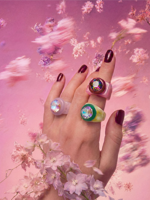 MOUNSER Spectrum Ring in Eyeshadow worn on model's hand — milky lavender limited edition cocktail ring with iridescent Austrian crystal on a pink floral background,  art object jewelry handcrafted to order in Los Angeles.