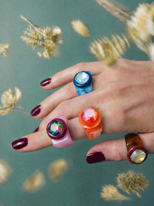 MOUNSER Spectrum Ring in Grapefruit worn on model's hand — milky deep orange limited edition cocktail ring with iridescent Austrian crystal on a green floral background,  art object jewelry handcrafted to order in Los Angeles.