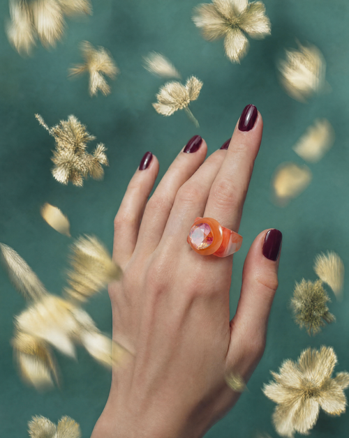 MOUNSER Spectrum Ring in Grapefruit worn on model's hand — milky deep orange limited edition cocktail ring with iridescent Austrian crystal on a green floral background,  art object jewelry handcrafted to order in Los Angeles.