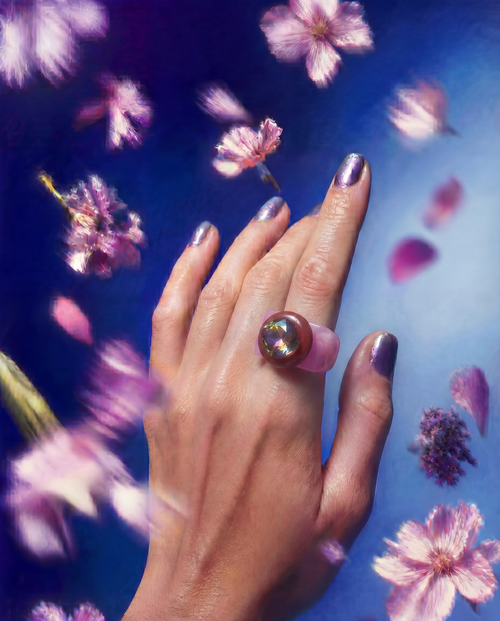 MOUNSER Spectrum Ring in Lip Gloss worn on model's hand — milky bubble gum pink limited edition cocktail ring with iridescent Austrian crystal on a blue floral background,  art object jewelry handcrafted to order in Los Angeles.